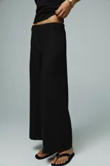 Pantalón negro de tiro medio con trabillas en la cintura, pernera recta y corte cropped. Cierre frontal con cremallera y ganchos metálicos.
