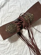 Faja ancha de cuero sintético color marrón con detalles metálicos dorados de estilo boho y cordones de ajuste con flecos.
