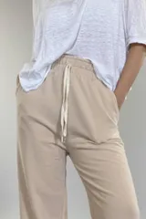 Pantalón de jersey color beige, de corte amplio, con bolsillos laterales y cintura elastizada con cordón ajustable.