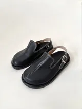 Zueco de cuero vacuno color negro, de punta cerrada y hebilla regulable en el talón.