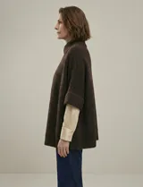 Capa o poncho tejido color verde esmeralda, con cuello polera alto que se cierra con un botón grande en el lateral. Presenta mangas cortas estilo japonesa y un calce amplio.