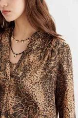 Camisa fluida con estampado reptil, escote redondo con apertura frontal y mangas largas terminadas en puño con botón.
