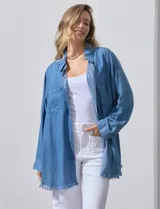 Camisa de jean celeste, marca Hester & Orchand, de corte oversize con cuello con solapa, escote en V y abertura central con botones. Delantera con bolsillos aplicados, mangas largas regulables con presilla y botón, y ruedo desflecado.