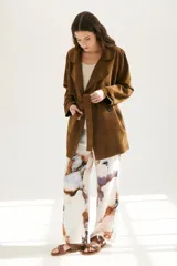 Trench simil gamuza color marrón, con cuello de solapa muesca, cuatro botones delanteros, bolsillos laterales y cinturón a la altura de la cintura.