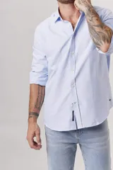 Camisa celeste a rayas verticales blancas, de corte clásico, manga larga y cuello abotonado.