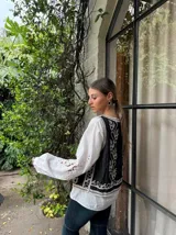 Chaleco negro con bordados florales blancos y ribete de crochet.