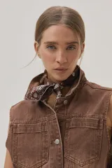 Chaleco largo marrón de algodón con cuello camisero, cierre frontal con botones, bolsillos laterales y lazo ajustable en la cintura.
