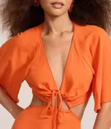 Vestido largo color naranja vibrante, con escote en V profundo que se anuda al frente, mangas amplias tipo mariposa y recortes laterales en la cintura.