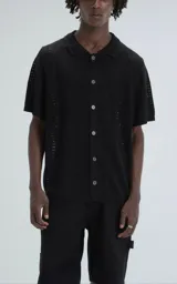 Camisa negra de tejido de punto calado con diseño de zigzag, cuello polo, manga corta y cierre frontal con botones.