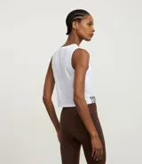 Musculosa deportiva corta (crop top) blanca, con cuello redondo y sisas amplias. Presenta un panel frontal de tela transparente/mesh sobre el busto y la palabra "SPORTY" estampada en color marrón en el bajo.