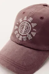 Gorra color crudo con visera y bordado frontal con el texto "Zara A Coruña Est. 1975 50 Years". Ajuste regulable en la parte posterior.