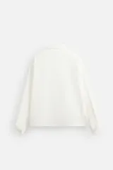 Camisa blanca de corte relaxed fit confeccionada en tejido de algodón y lino. Tiene cuello bowling, manga larga con puños abotonados, jaretas en el delantero, bolsillos de parche en pecho y cadera, bajo con aberturas laterales y cierre frontal con botones.