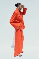 Pantalón de vestir color naranja, de tiro alto y pernera ancha. Presenta doble pliegue frontal, trabillas en la cintura, bolsillos laterales y falsos bolsillos de vivo en la espalda.