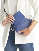 Cartera tipo bandolera Tahari, color azul, con silueta de media luna y textura granulada. Incluye un monedero/tarjetero a juego que se integra en el bolsillo frontal. Tiene una cadena decorativa de eslabones plateados.
