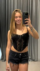 Corset negro con encaje y lentejuelas, con tirantes finos y cierre frontal con cremallera.