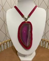 Collar con dije grande de piedra natural fucsia con borde marrón, engarzada en cuero fucsia y colgante de cinta de cuero fucsia con herrajes dorados.