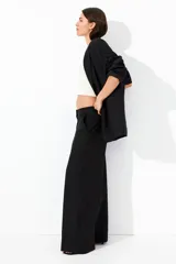 Pantalón negro de corte ancho, tiro alto, con bolsillos al bies y cierre oculto.