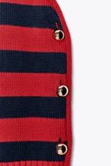 Chaleco de punto rojo con rayas horizontales azul marino y botones dorados decorativos en los laterales. Cuello redondo y sisa amplia.
