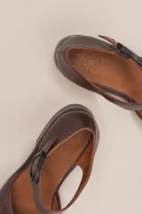 Zapato marrón de cuero vacuno trenzado a mano, con correa al tobillo con hebilla negra y suela de cuero.