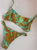 Bikini de dos piezas con estampado de hojas en tonos verde menta y mostaza. El corpiño es tipo top con tirantes finos y tazas soft removibles. La bombacha es colaless con frunces ajustables en los laterales.