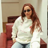 Canguro oversize color crudo con capucha y cordones ajustables. Estampado en la espalda con tres flores rojas, la frase "Lookmom Street" y un texto motivacional.
