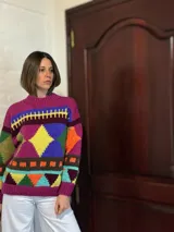 Sweater de lana merino color crema con cuello alto y diseño con motivos geométricos en amarillo, naranja, violeta y negro.