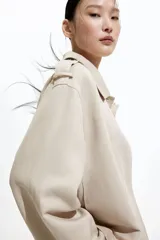 Chaqueta corta color beige, de corte oversized, con cuello clásico, charreteras abotonadas, bolsillos laterales y trabilla con botón en los puños.