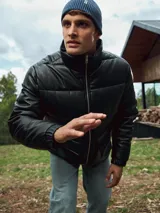 Campera puffer negra de cuero sintético con cuello alto, cierre frontal con cremallera, bolsillos delanteros con solapa y puños elásticos.