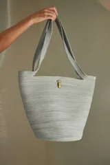 Bolso tipo tote confeccionado en soga de algodón color crudo, con asas de hombro y broche de bronce.