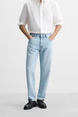Pantalón de jean celeste de corte slim fit y tapered, con cinco bolsillos, efecto lavado y cierre frontal con cremallera y botón.