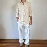 Camisa de lino color beige, de corte oversize, con cuello clásico y mangas largas con puños abotonados.