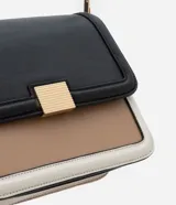Cartera mediana de PU color negro, con asa transversal regulable, detalle metálico dorado en el frente y recortes contrastantes en beige y blanco.