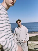 Polo de manga larga gris claro con cuello tipo camisa y cierre parcial con botones. Corte holgado y puños de canalé.