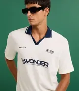 Remera de manga corta con cuello polo contrastante en azul marino y abertura en V. El cuerpo de la prenda es color crema y lleva un estampado frontal con la palabra "WONDER".