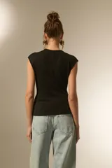 Top negro sin mangas, con escote en V cruzado y detalle de botones laterales. Presenta un corte ajustado al cuerpo con un diseño asimétrico en el ruedo.