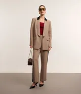 Blazer de tejido plano color beige con estructura de sastrería, cuello smoking con contraste negro en la nuca, botón único para cierre y solapas delanteras que simulan bolsillos.