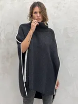 Poncho tejido de punto grueso color gris con cuello alto y aberturas laterales con ribete blanco.
