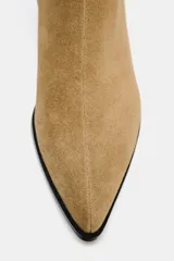 Botín de mujer de caña media color beige, confeccionado en serraje con detalle de pespuntes en la parte delantera. Tiene tacón bloque medio y cierre mediante cremallera lateral.