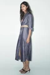 Vestido camisero azul con cinturón de rafia, de cuello solapa y manga tres cuartos con trabilla y botón. Tiene bolsillos de parche en el delantero y cierre frontal con botones.