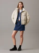Campera puffer color beige claro con logo de Calvin Klein bordado en el pecho. Tiene cuello alto, cierre con cremallera y botones a presión, bolsillos laterales y puños elásticos.