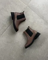 Botines Chelsea de cuero marrón con elástico negro en los laterales y suela de goma negra.