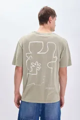 Camiseta manga corta oversize color verde con estampado de una pieza de rompecabezas con una flor en su interior y la palabra 'Island' debajo.