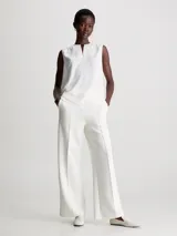 Pantalón blanco de pierna ancha confeccionado en tejido de punto técnico con poliéster reciclado y elastano. Presenta talle medio, pinzas delicadas en el centro de la pierna, bolsillos con ranura y barra de metal con logo de Calvin Klein debajo de la cintura.