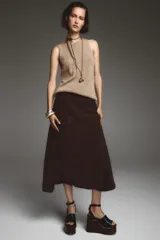 Falda midi de tiro alto confeccionada en ante color marrón chocolate, con bolsillos delanteros y traseros, abertura frontal y cierre con cremallera y botón.