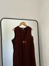 Vestido largo sin mangas, color marrón oscuro, con escote redondo y corte amplio. Presenta bolsillos laterales.