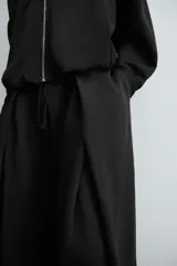 Pantalón jogger negro de corte relaxed fit, confeccionado en tejido de algodón. Presenta cintura elástica ajustable con cordón, pliegues frontales, bolsillos delanteros y un bolsillo trasero.
