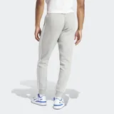Pantalón de jogging Adidas Adicolor 3 Rayas, color gris con las tres rayas blancas a los costados. Cuenta con puños acanalados, bolsillos laterales con cierre, cintura elástica con cordón de ajuste y logo bordado.