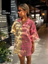 Camisa oversize de manga corta con cuello camisero, confeccionada en tejido de viscosa y lino. Presenta un diseño estampado de estilo patchwork, dividido verticalmente en dos mitades: una en tonos amarillos y marrones, y la otra en tonos rosados y morados.