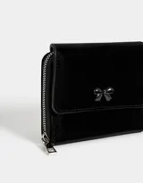 Billetera pequeña de cuerina color negro con cierre de cremallera y broche. Presenta un moño metálico en el frente.