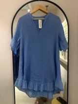 Vestido corto de lino color celeste, con escote en V y cuello mao, mangas cortas con volados y ruedo con volado.